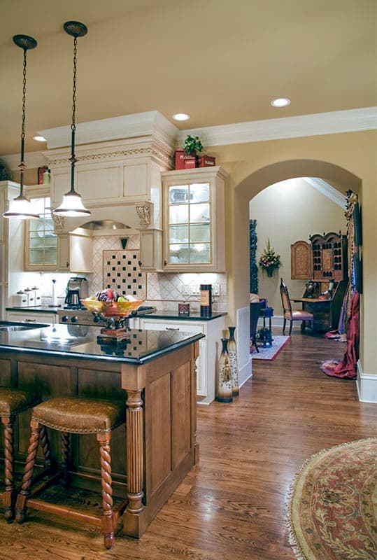 Kitchen island with granite countertop and seating, decorative range hood with cabinetry, archway to dining area.