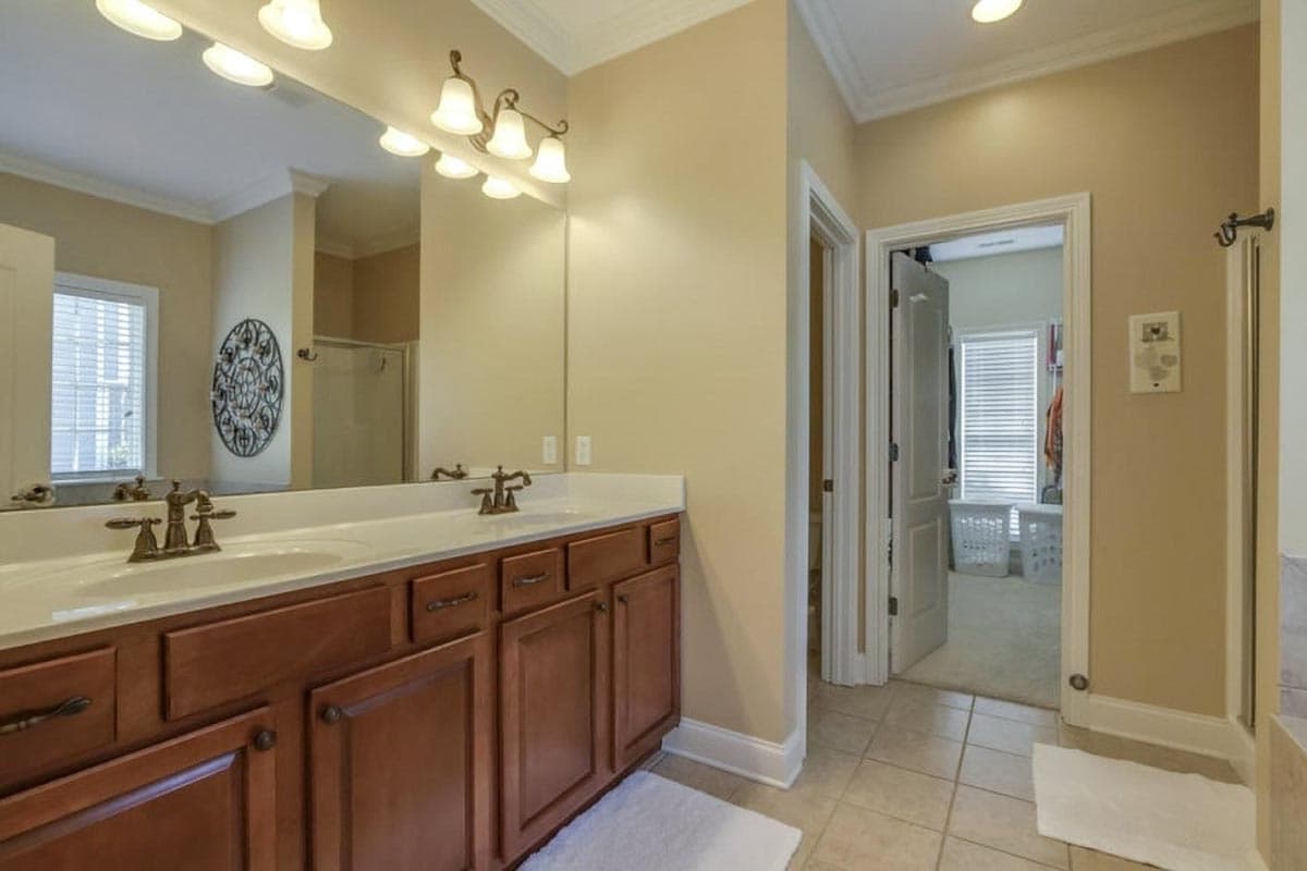 Bathroom featuring double vanity with dark wood cabinets, a large mirror, and doorway to a walk-in closet.