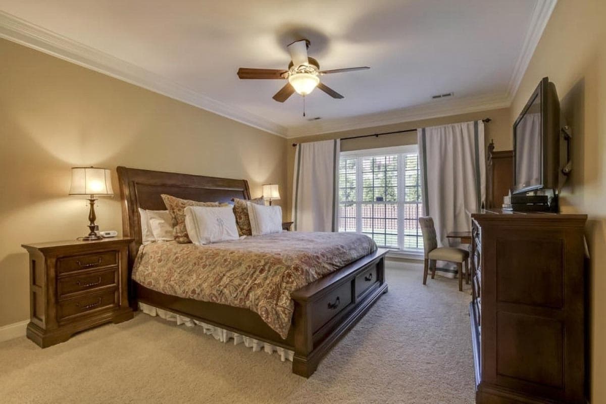 Bedroom with king bed, two nightstands, dresser with television, and large window with white curtains.