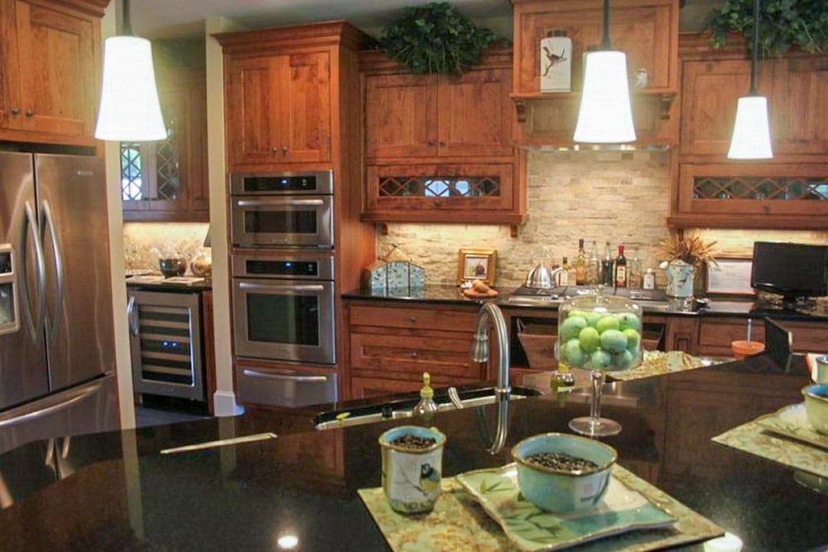 Kitchen with cherry wood cabinets, double ovens, stainless steel refrigerator, wine fridge, and a granite island.