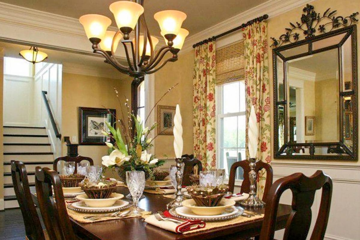 Dining room with dark wood table set for four, ornate chandelier, floral curtains, and a mirrored wall.