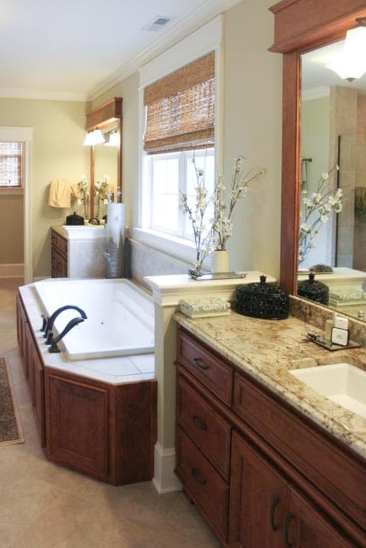 Corner jetted tub with dark wood cabinetry and granite countertop vanity with white sink and large mirror.