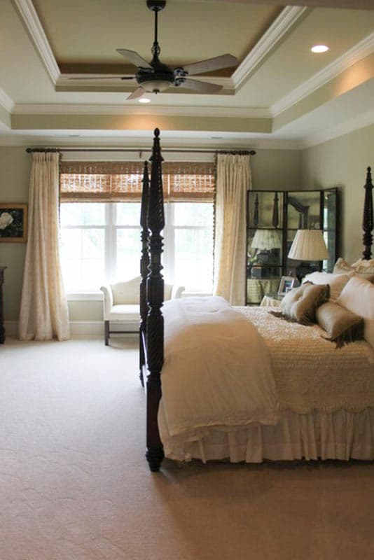 Bedroom interior featuring a four-poster bed, coffered ceiling with fan, and large window with seating nook.
