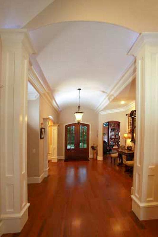 Interior view of grand foyer with arched ceiling, double front doors, hardwood floor, and decorative columns.