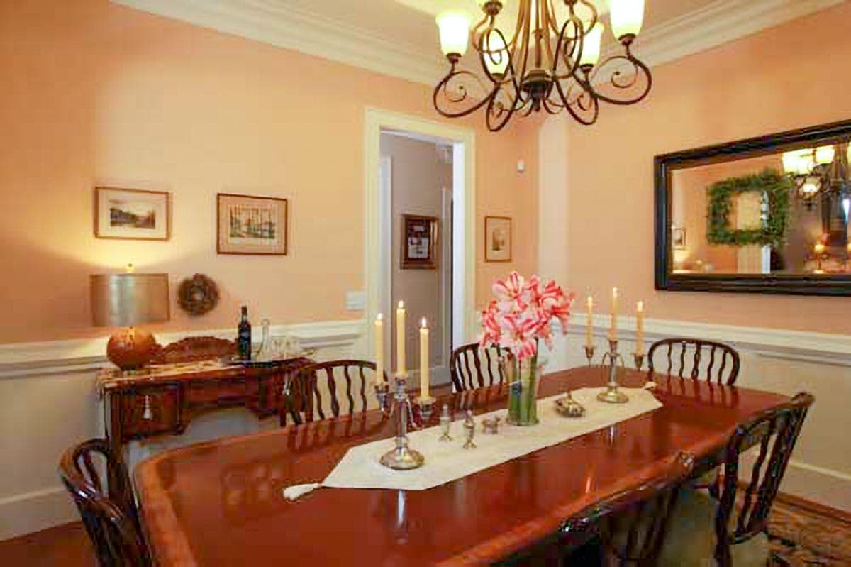 Dining room with wooden table set for four, ornate chandelier, and a large mirror over a console table.