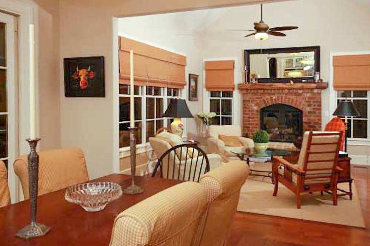 Interior view of a great room with a brick fireplace, vaulted ceiling, large windows, and seating area.