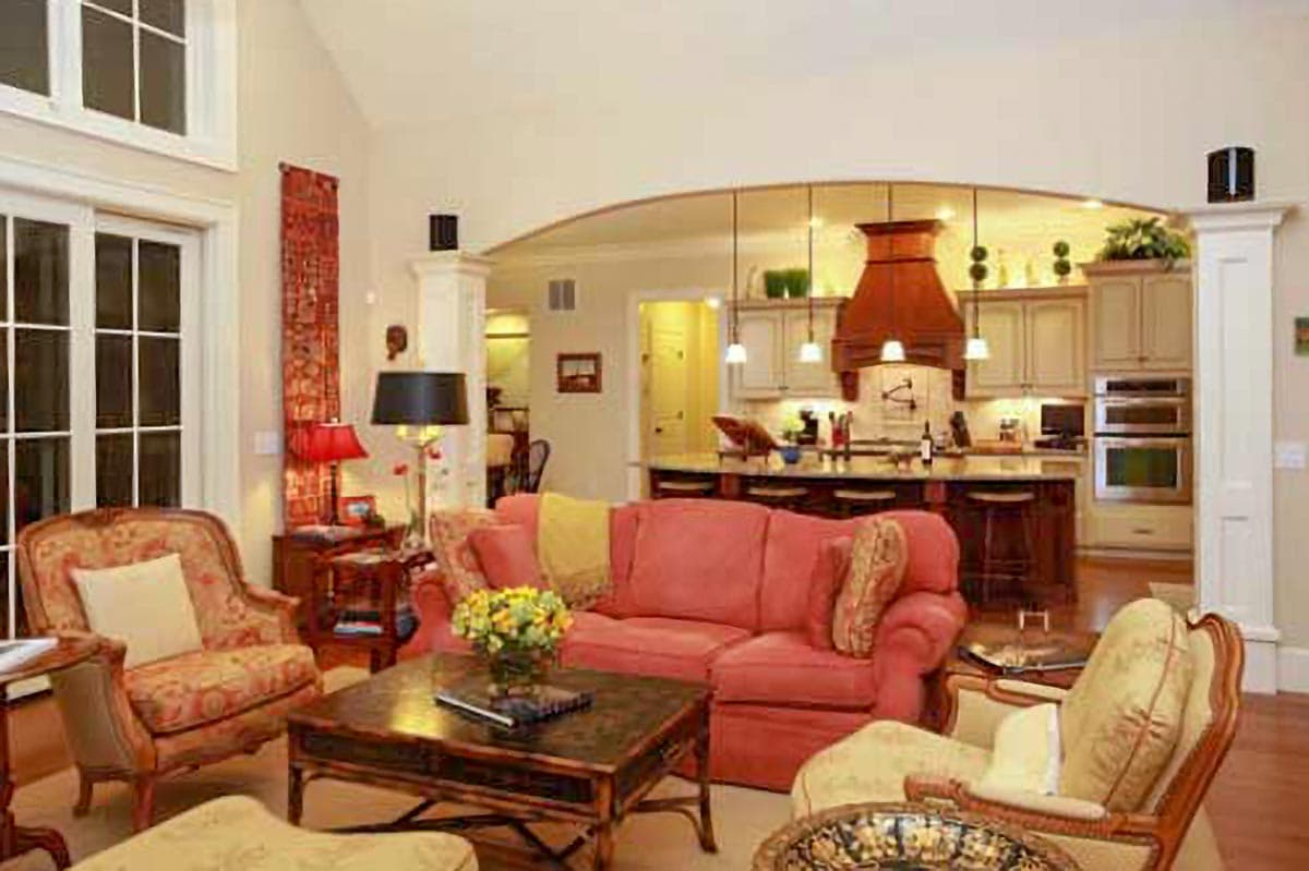 Interior rendering of open-concept living room with kitchen, featuring arched entry, island, and large windows.