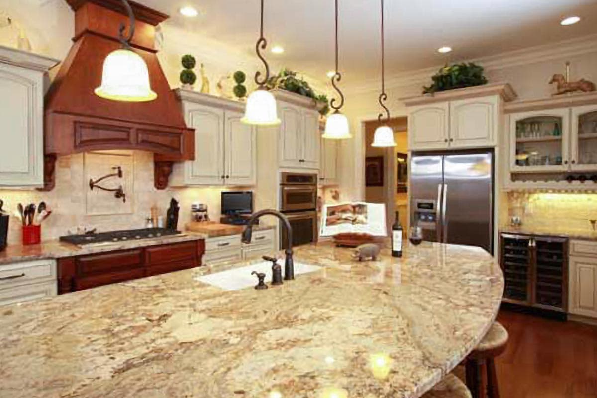 Kitchen interior with large granite island, wood vent hood over gas range, double ovens, and stainless steel refrigerator.