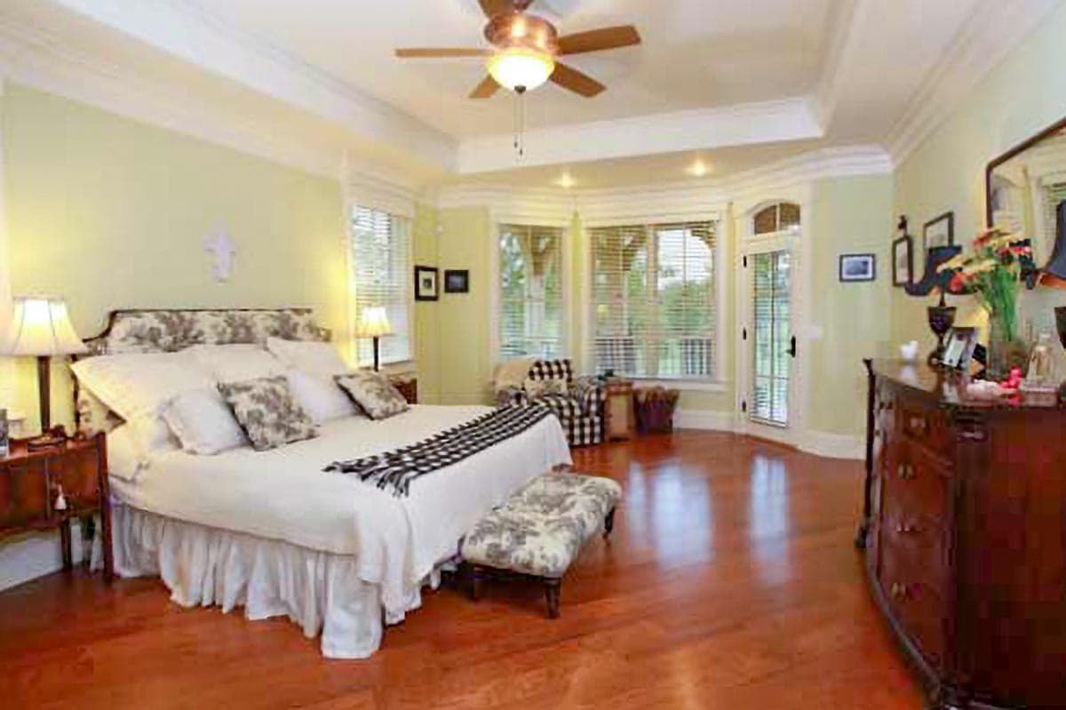 Bedroom with tray ceiling, bay window, door to exterior, and wood floors.