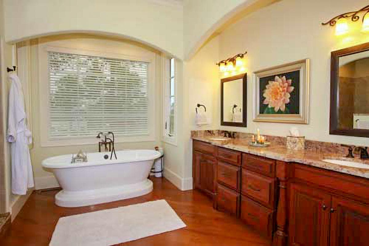 Bathroom interior with freestanding tub, large window, and double vanity with wood cabinets and granite countertops.