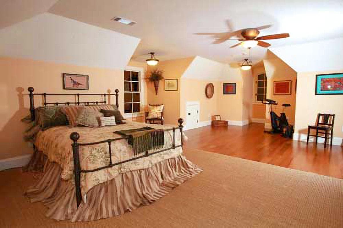 Interior view of a bedroom with a wrought-iron bed, sloped ceilings, wood floors, and exercise equipment.