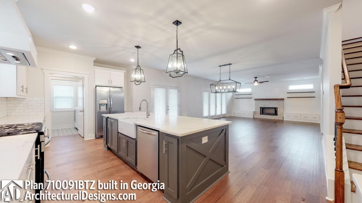 Open-concept living area with kitchen island, fireplace, built-in shelving, and staircase.