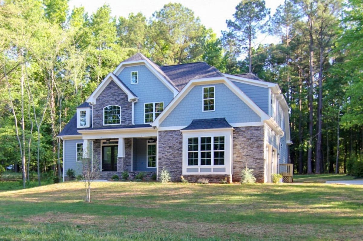 House plan exterior. Two-story home with stone and shingle siding. Features include multiple gables, a front porch, and large windows.