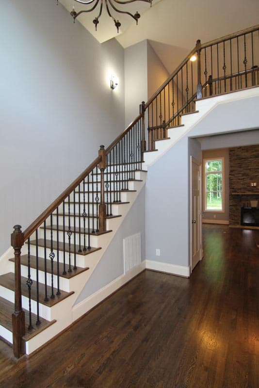 Interior view of a grand staircase with dark wood railings, wrought iron spindles, and a two-story landing.