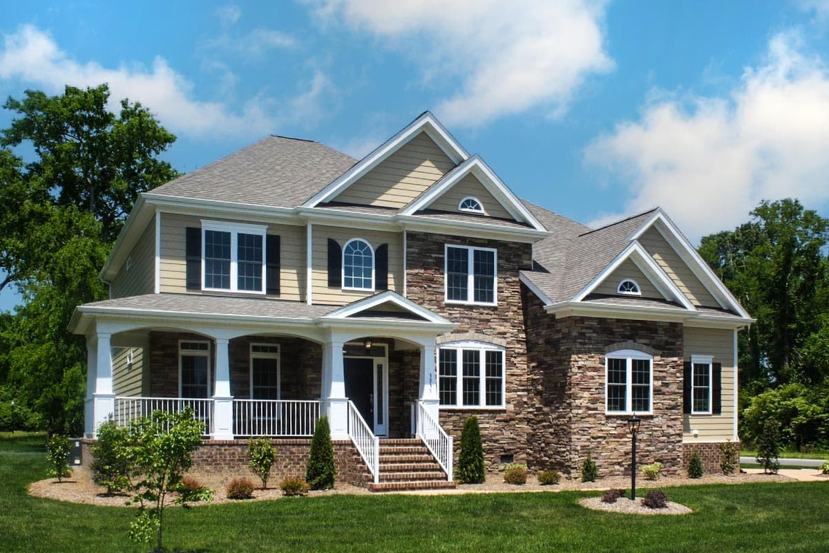 House plan exterior with two stories, a front porch with columns, gables, and a stone facade on a portion of the exterior.