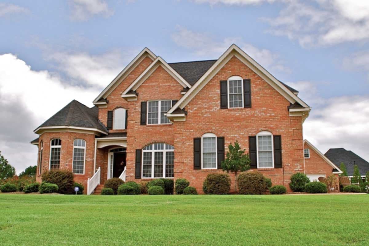 House plan exterior. Two-story brick home with gabled roof, multiple dormers, and a rounded bay. Features include black shutters and a porch.