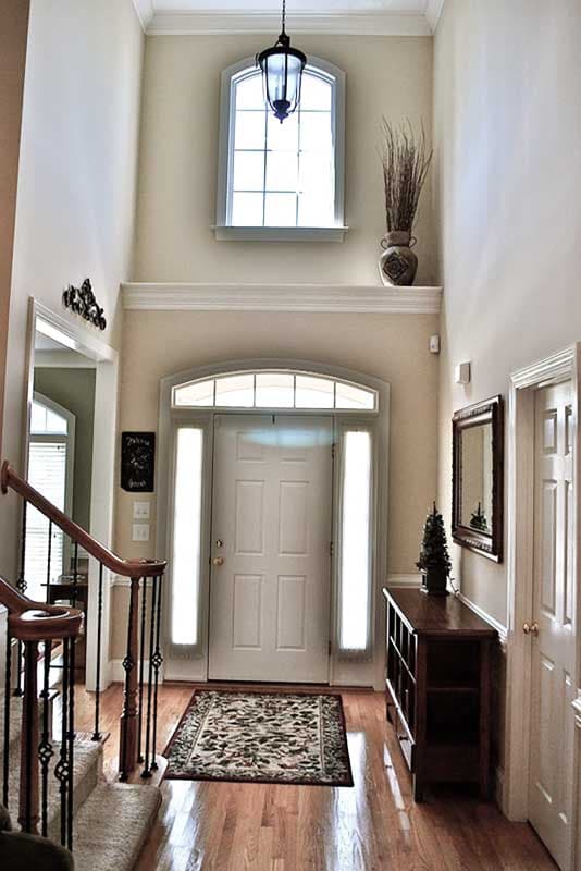 Interior foyer with arched transom window above door, staircase with wood banister and metal spindles, and hardwood flooring.