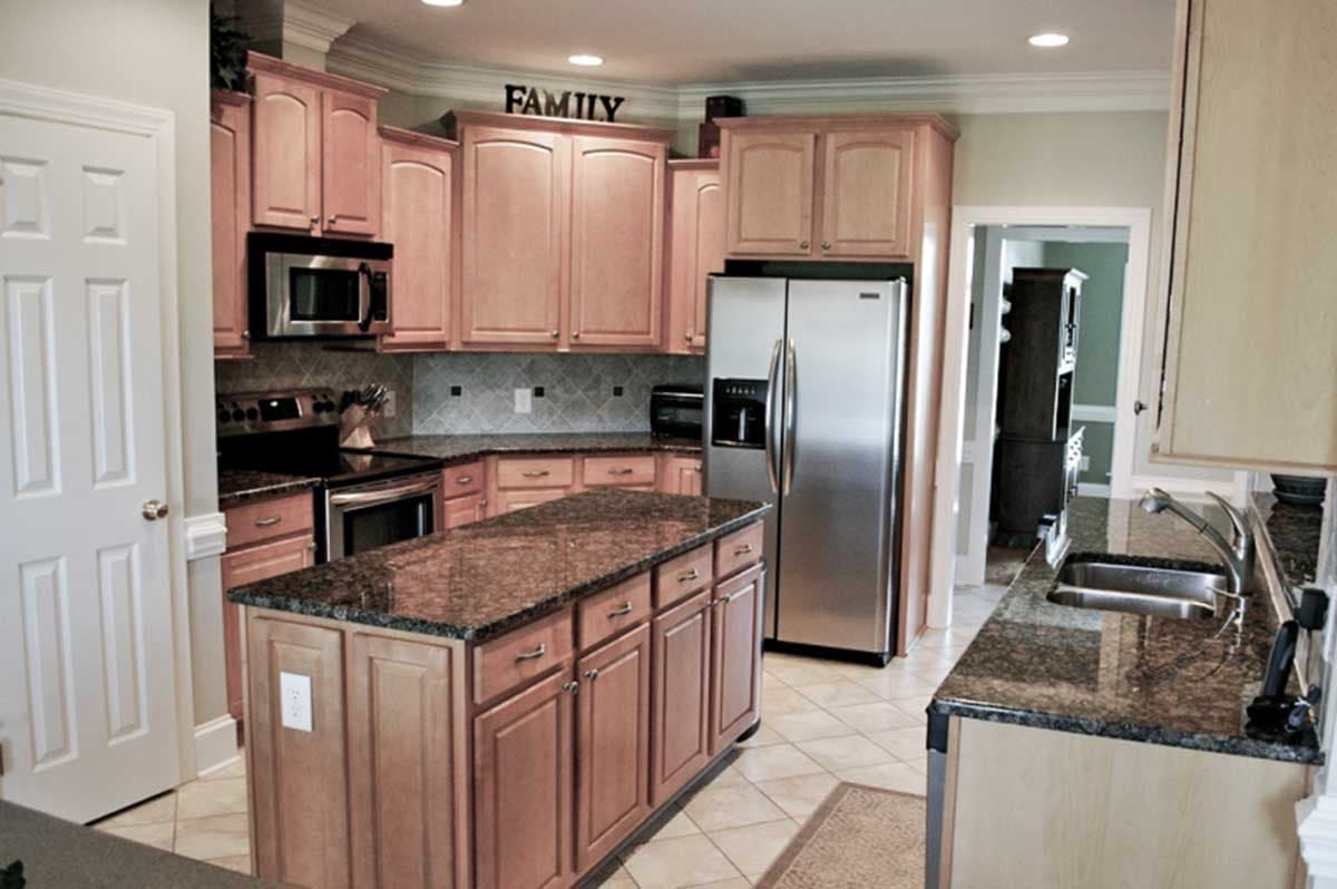 Kitchen with light wood cabinets, granite countertops, stainless steel refrigerator, island with sink, and tile flooring.