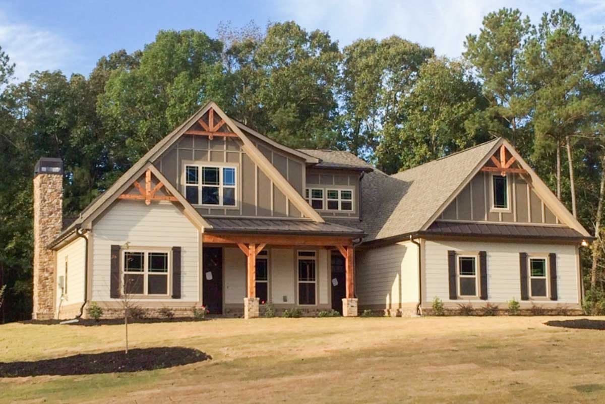 Modern farmhouse house plan exterior with prominent gables, exposed wood beams, stone chimney, and covered porch.