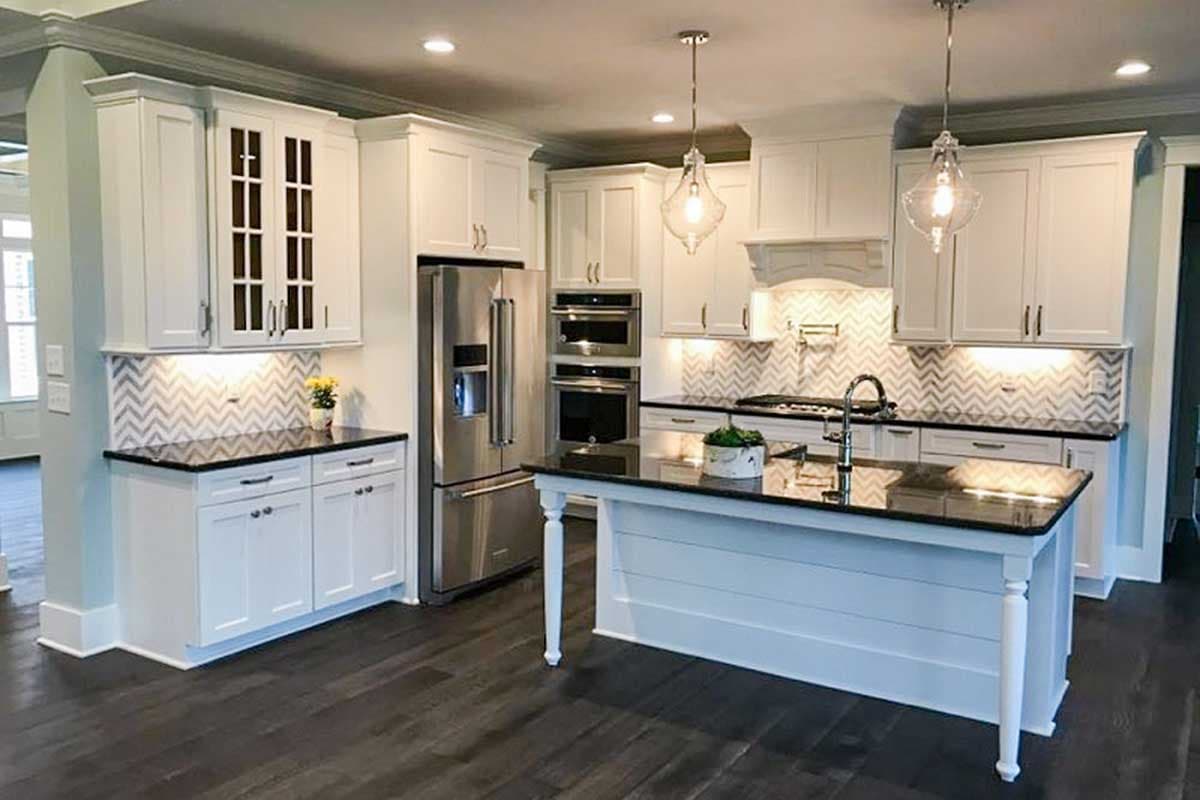 Kitchen featuring white cabinets, stainless steel appliances, a large island with sink, and chevron tile backsplash.