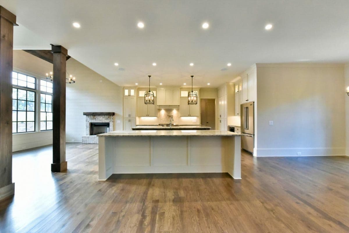 Open concept living area with large island, kitchen with shaker cabinets, and fireplace with brick surround.