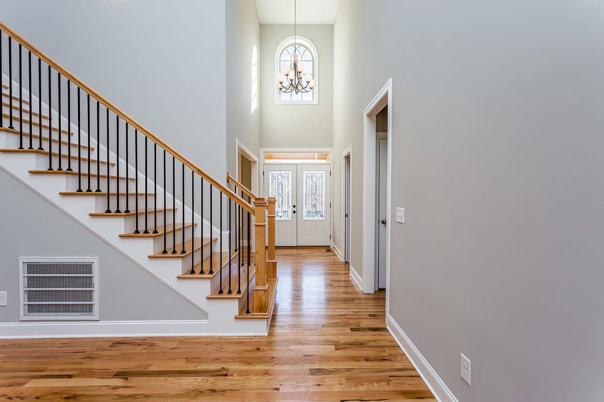 Interior view of a foyer with a grand staircase, double entry doors with glass, and a chandelier.