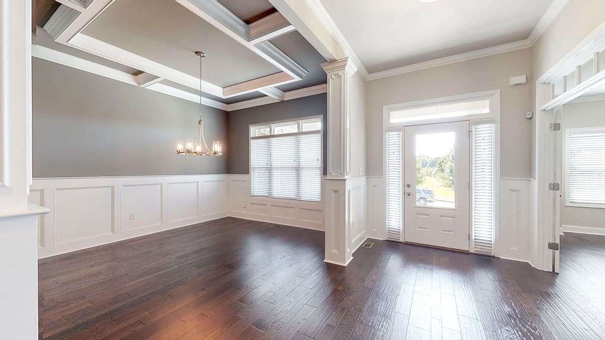 Interior view of dining room with coffered ceiling, wainscoting, chandelier, and entry door.