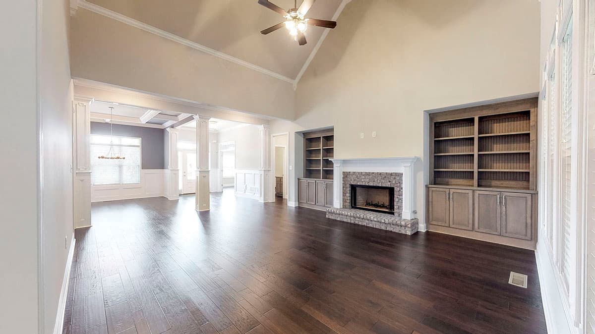 Great room with vaulted ceiling, brick fireplace, built-in bookshelves, and open doorway to dining area.