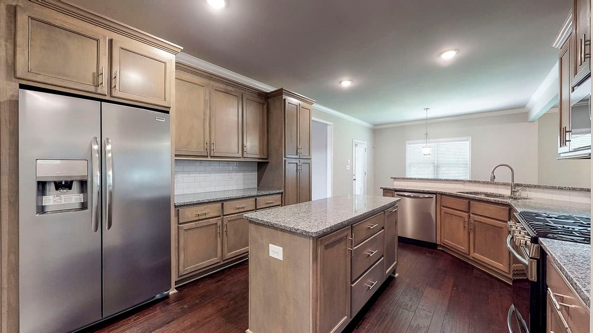 Kitchen interior with stainless steel refrigerator, granite countertops, wood cabinets, and island with drawers.