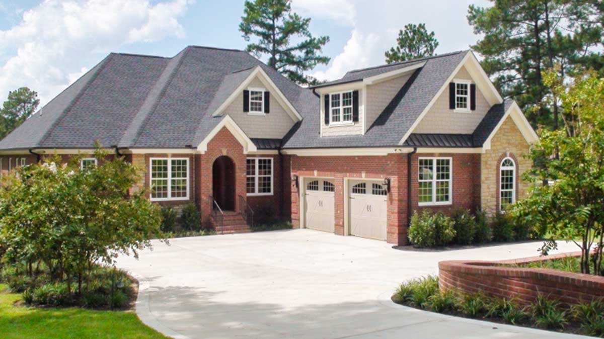 House plan exterior. Two-story brick home with gabled roof, dormers, and attached two-car garage. Features arched entry and stone accents.