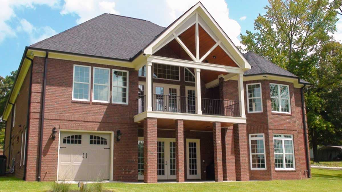 House plan exterior: Brick two-story home with a covered second-story balcony, prominent gables, and a two-car garage.