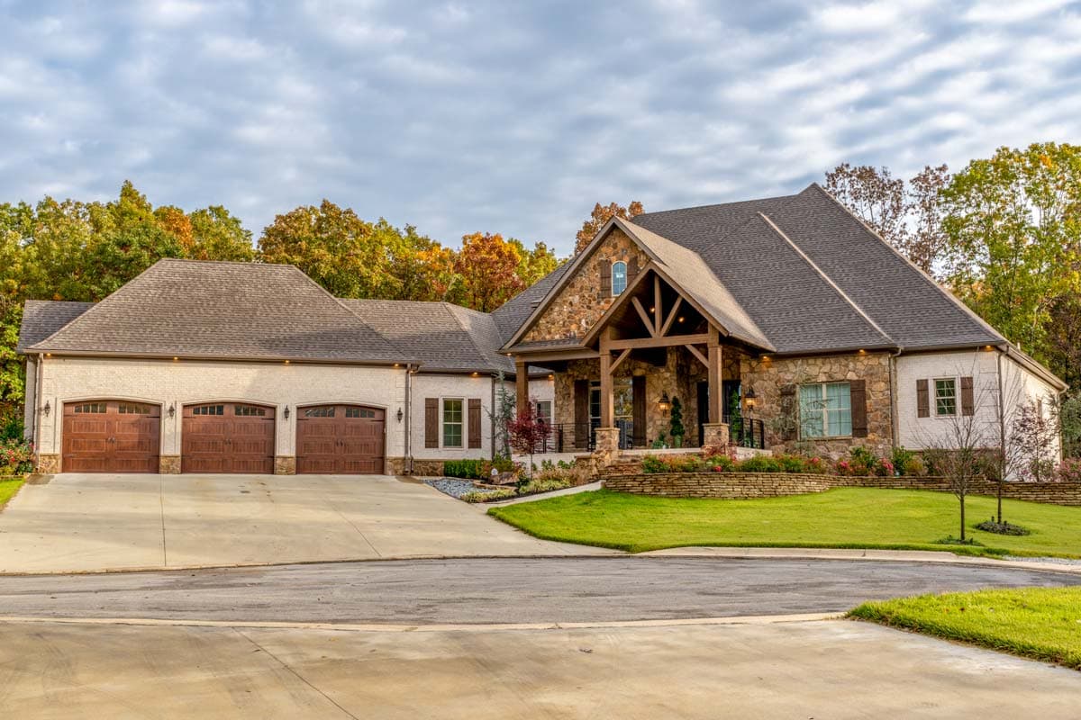 House plan exterior. Two-story Craftsman home with a stone and stucco facade, a gable roof, and a covered porch. Features a three-car garage.