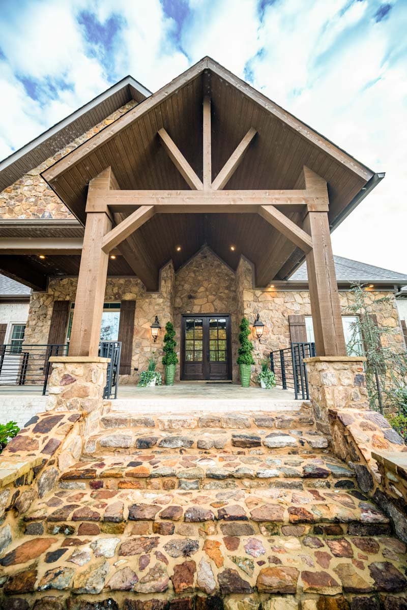 House plan exterior with stone facade, covered porch with exposed timber framing, and wide stone steps.