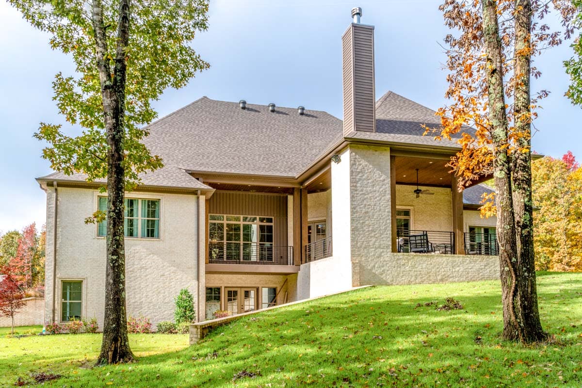House plan exterior: Two-story brick home with covered porch, large windows, and prominent chimney.