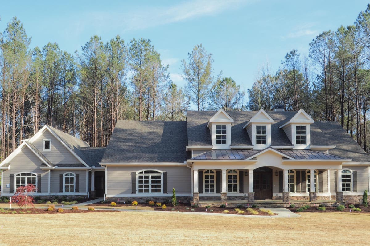House plan exterior: Ranch-style home with a prominent covered front porch supported by columns, multiple dormers, and stone accents.