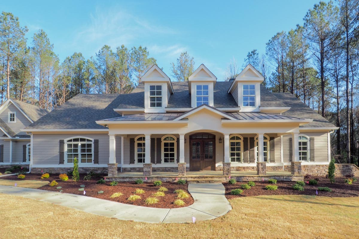 House plan exterior: One-and-a-half story home with wraparound porch, dormer windows, arched entry, and stone accents.