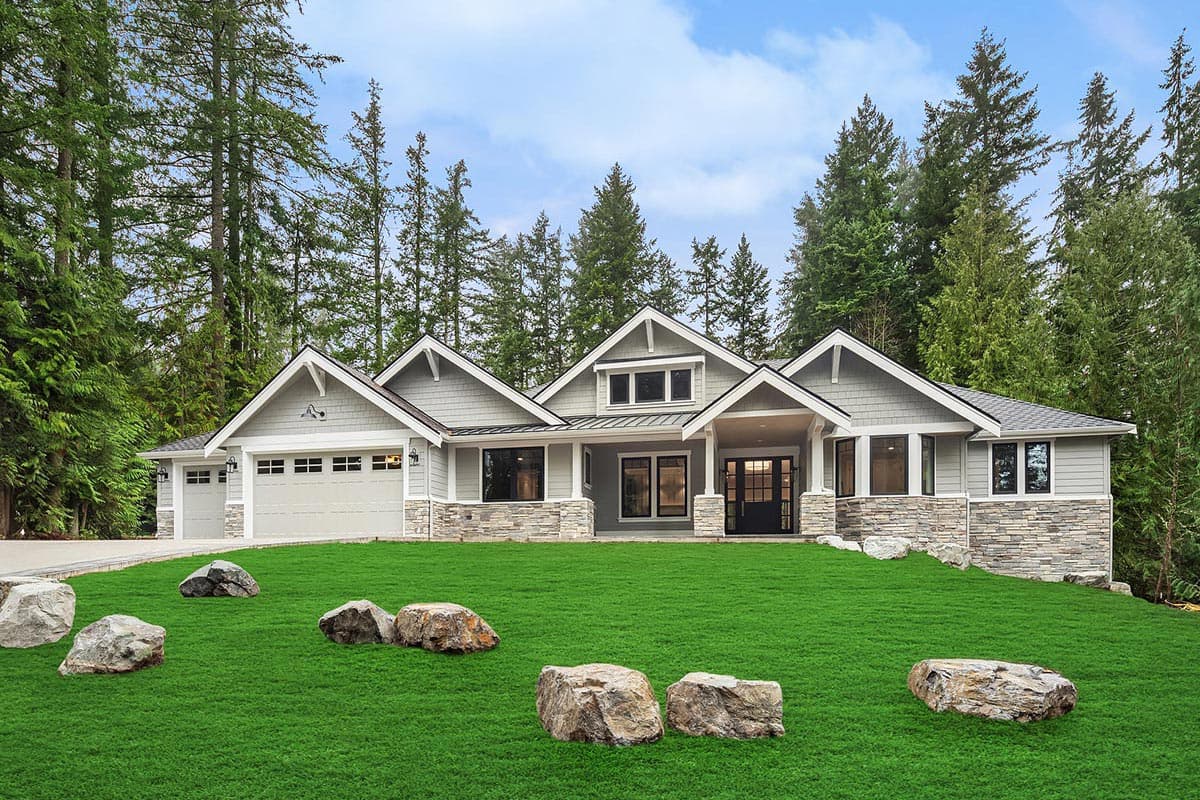 Modern Ranch house plan exterior with a wide covered entrance, three garage bays, stone accents, and multiple gables.