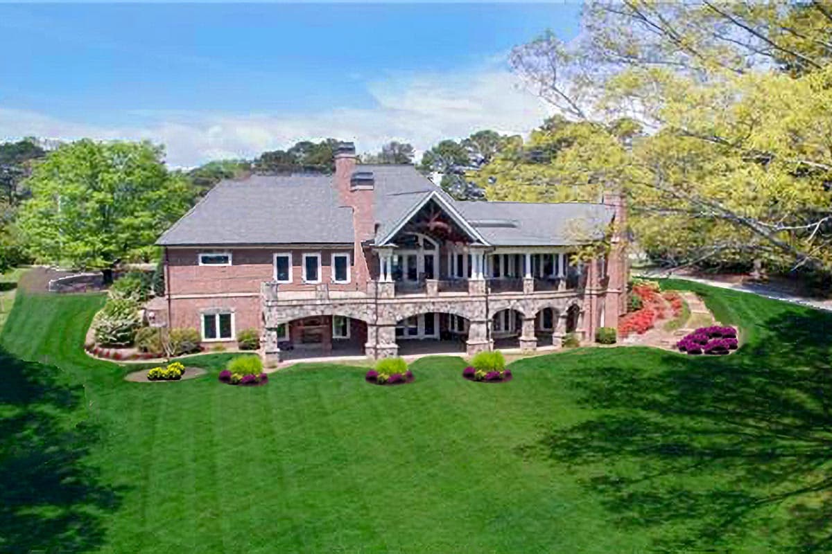House plan exterior: Two-story brick residence with arched stone loggia, covered porch, and prominent gabled dormer.