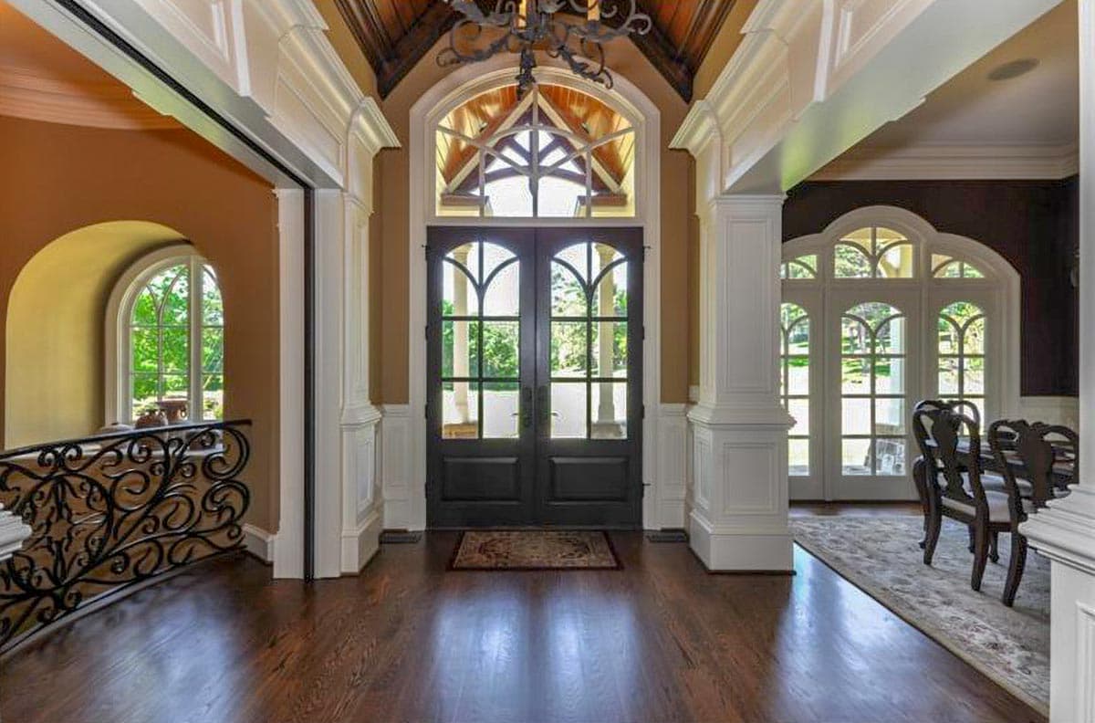 Interior view: Grand foyer with double front doors, arched windows, coffered ceiling, and ornate iron railing.