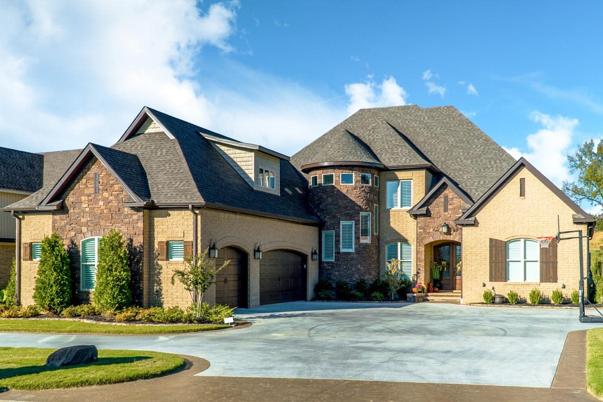 House plan exterior. Two-story home with a stone and brick facade. Features include a turret, multiple gables, and an arched garage entry.