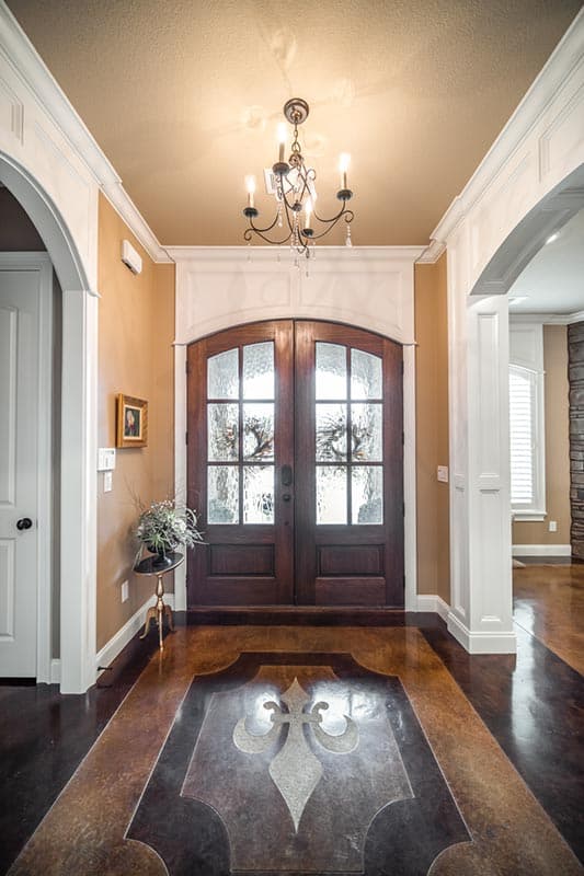 Entryway with arched double doors, decorative floor inlay, and chandelier.