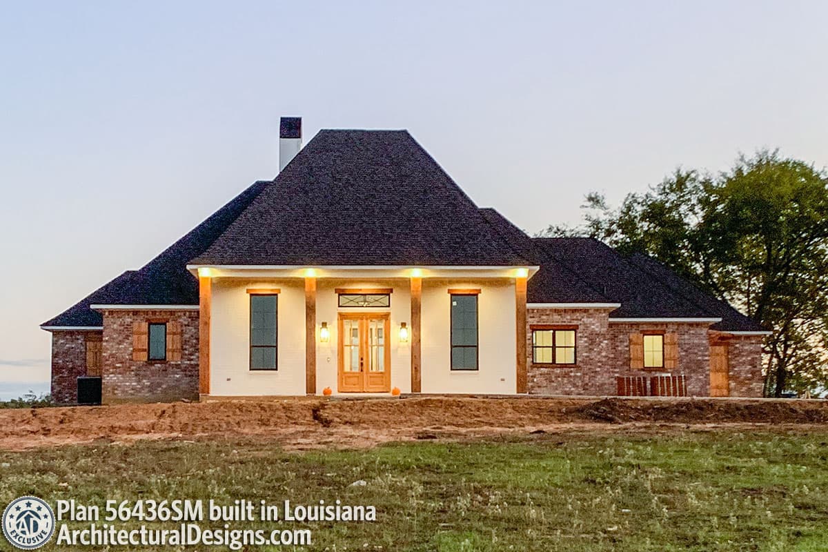 House plan exterior: One-story Modern Farmhouse with brick accents, wide front porch supported by wooden beams, and a prominent central gable.