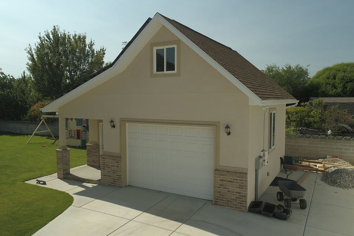 House plan exterior with attached garage, gable roof, dormer window, and covered entrance supported by brick columns.