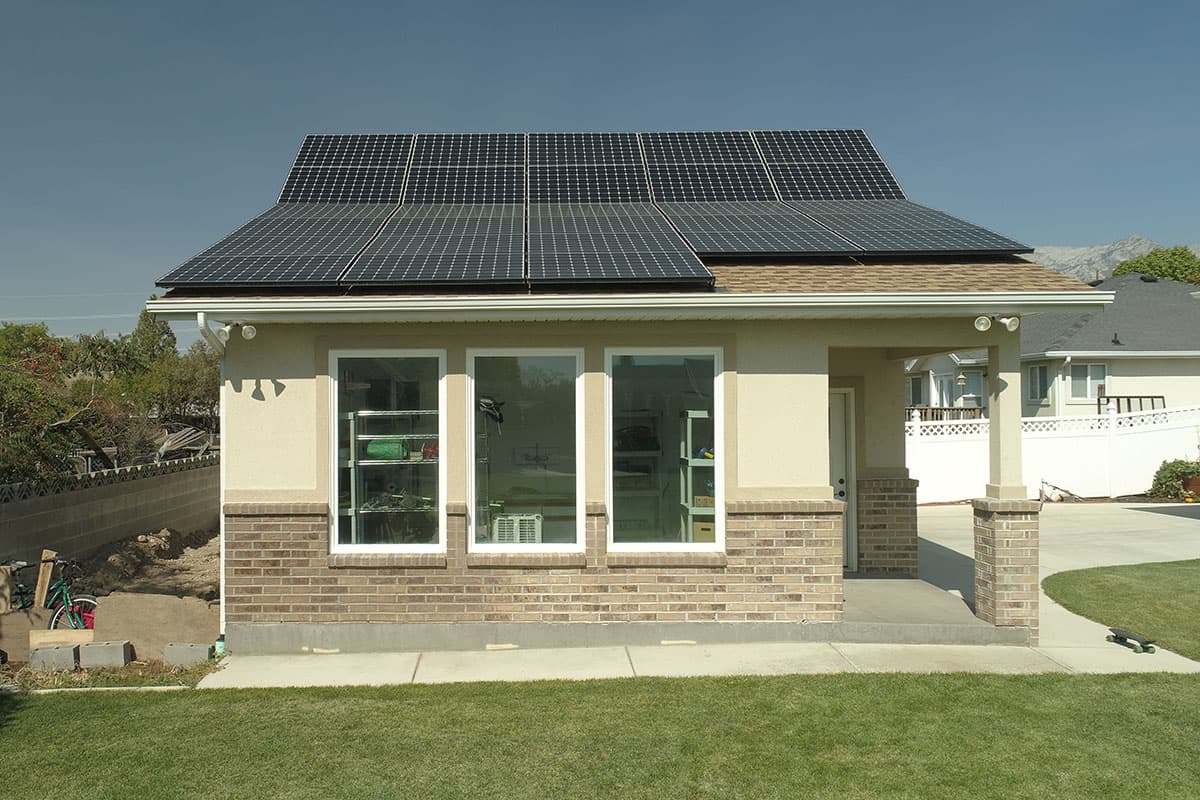 House plan exterior with solar panels on roof, three large windows, and brick and stucco finish. Porch with column.