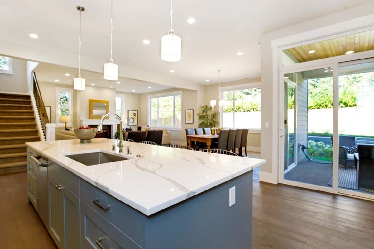 Open concept interior view shows kitchen island with sink, dining area, living room, stairs, and patio access.