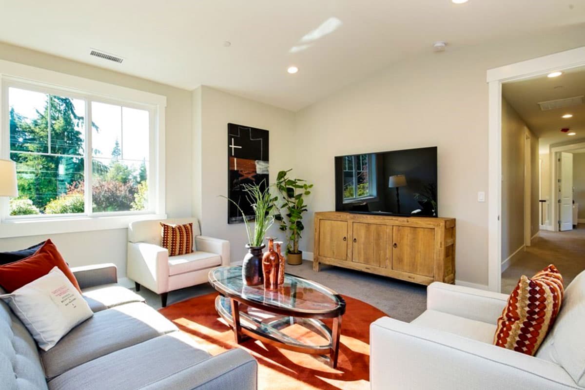 Living room with sectional sofa, accent chairs, wood media console, large window, and hallway view.