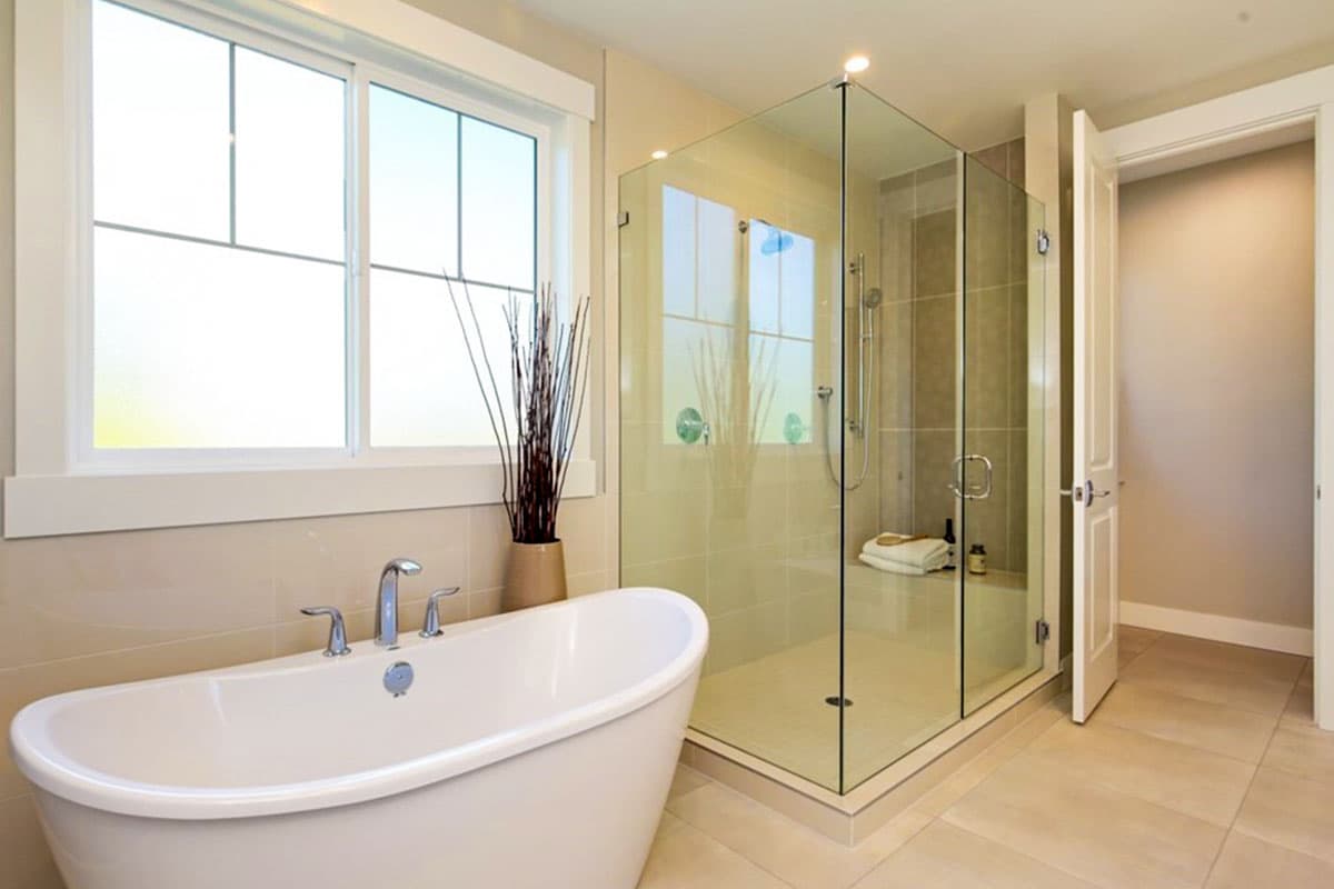 Modern bathroom with freestanding tub, glass-enclosed shower with chrome fixtures, and large window.
