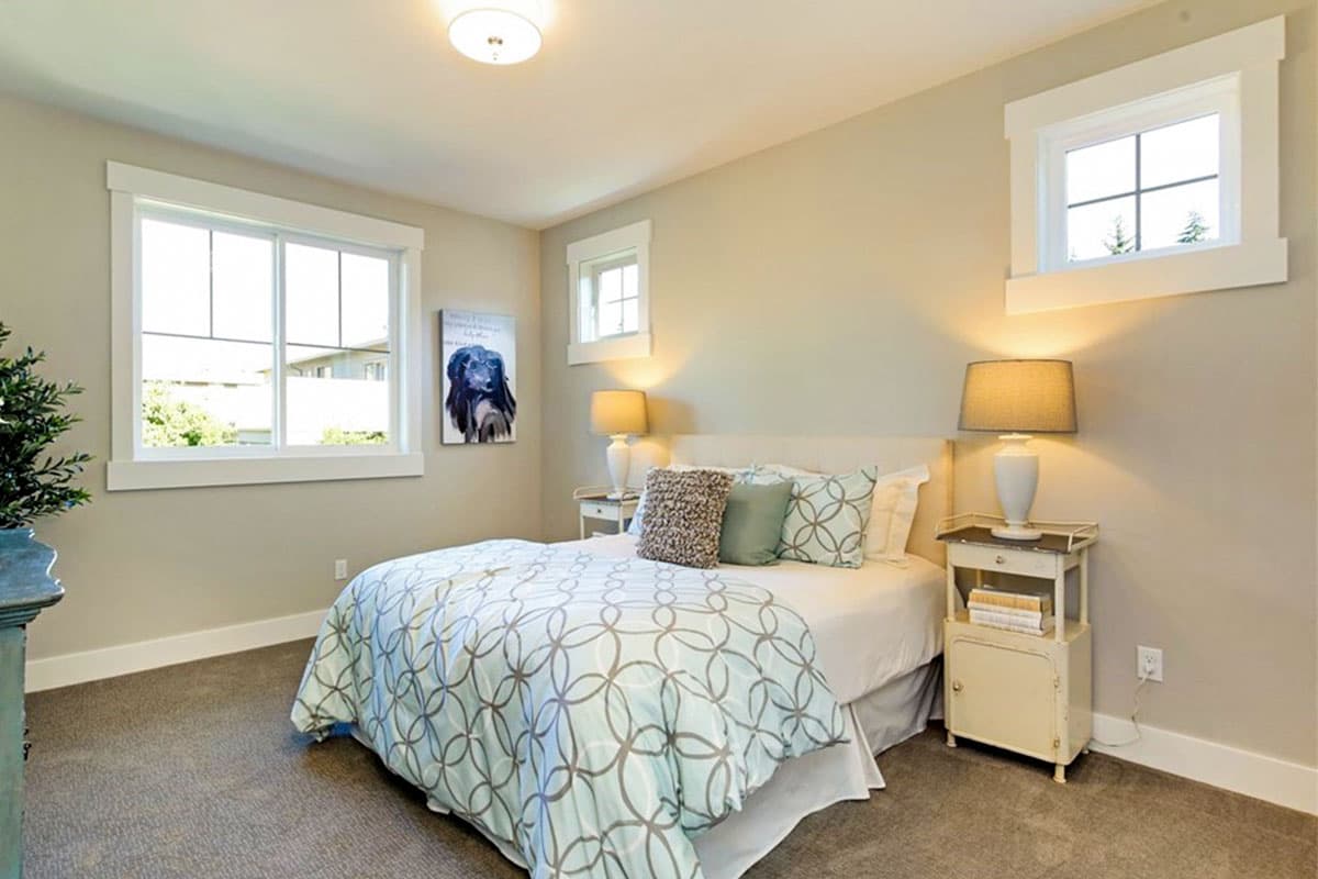 Bedroom interior with a bed, two nightstands with lamps, and three windows with white trim.