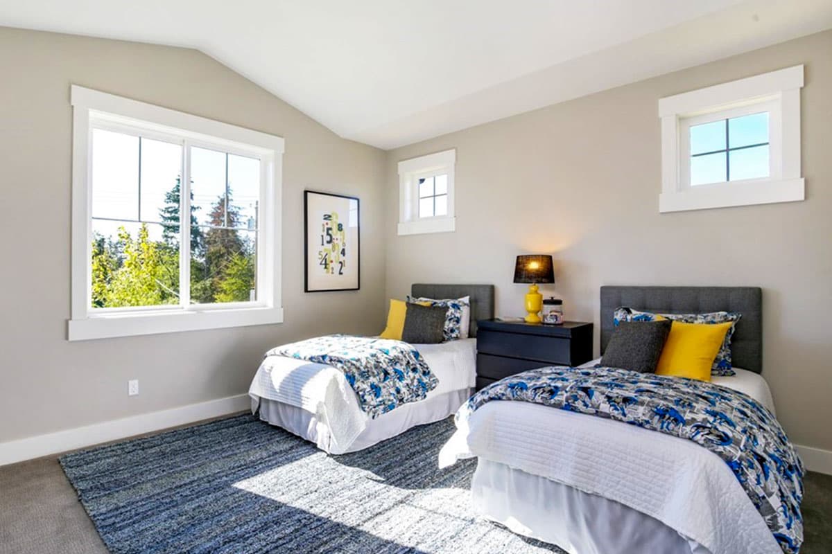 Bedroom with vaulted ceiling, two twin beds with patterned comforters, and large windows.
