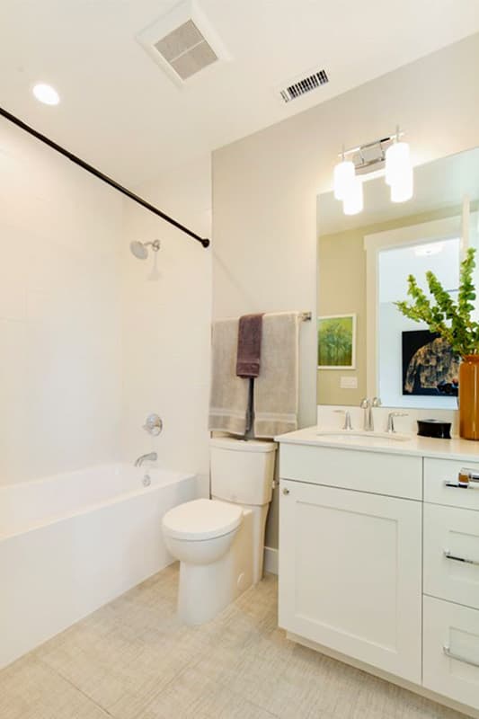 Modern bathroom with white tub, toilet, vanity with white quartz countertop, and light wood-look tile floor.